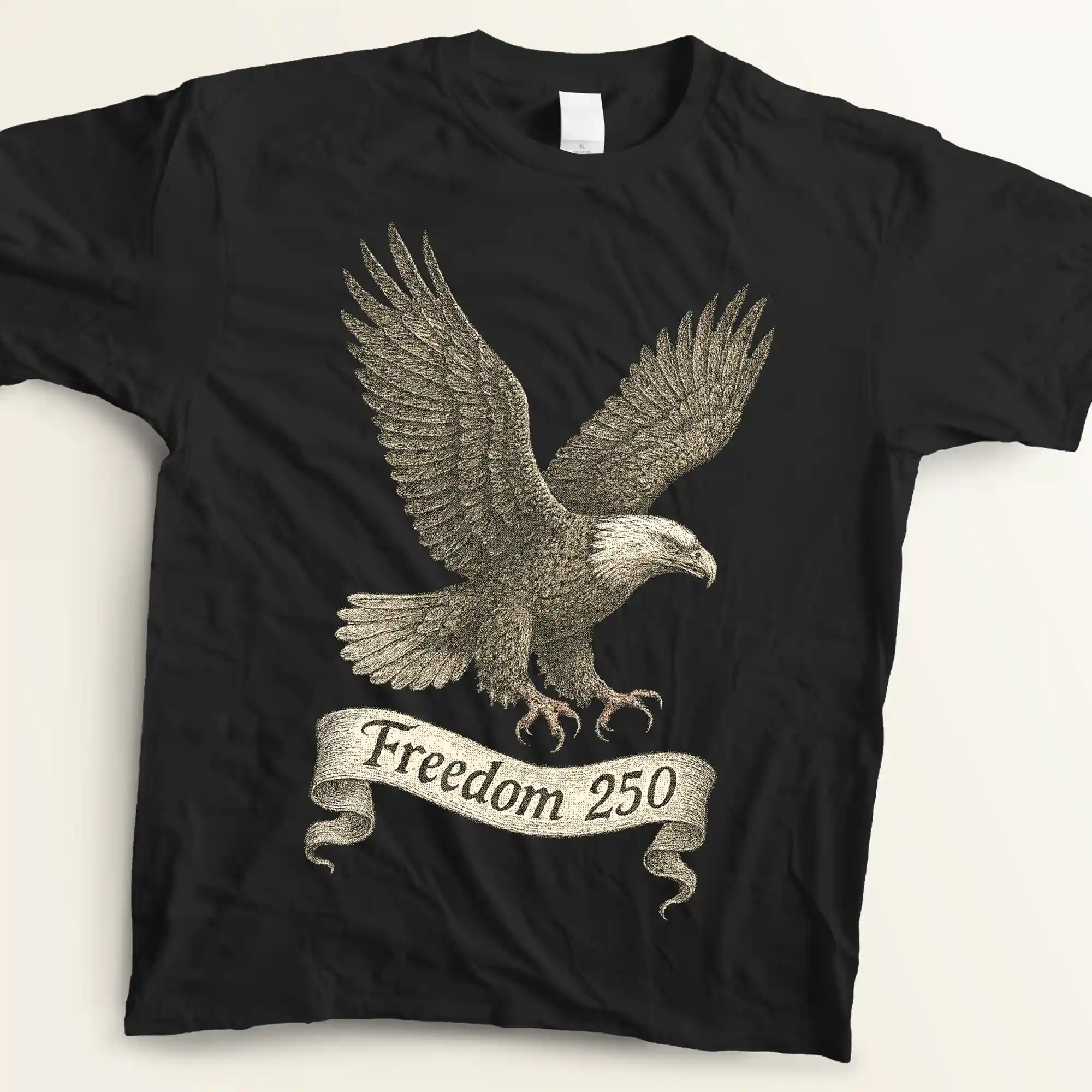 Flat lay view of a black graphic t-shirt resting on an off-white background. The shirt displays a highly detailed vintage engraving of a bald eagle soaring with its wings spread wide, rendered with fine cross-hatching in charcoal and antique white shades. An elegant, flowing banner underneath features the text "Freedom 250" written in a slightly distressed cursive script.