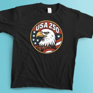 A flat lay view of a black graphic t-shirt spread evenly across a bright blue surface. The shirt features a large, central circular badge design with a bold 1970s retro aesthetic. Inside the circle, a detailed illustration of a bald eagle head is surrounded by an American flag motif with stars and stripes in red, white, blue, and gold. The text "USA 250" is boldly curved across the top of the emblem in a blocky, off-white font.